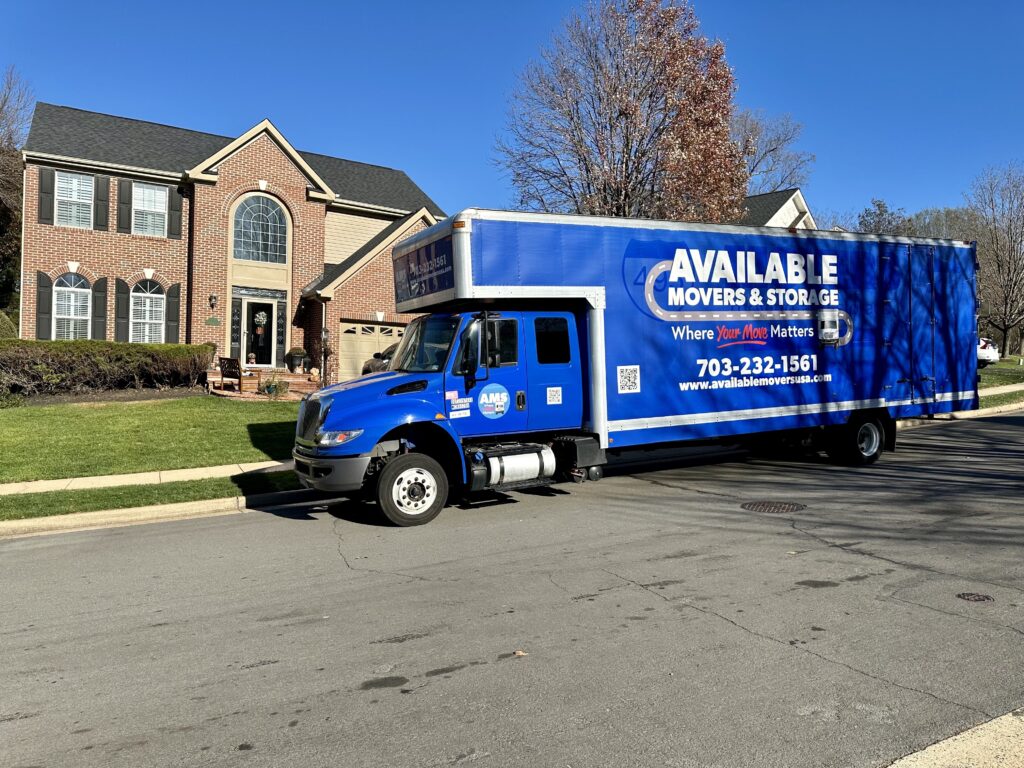 Blue moving truck with Available Movers & Storage logo, in front of a brick home.
